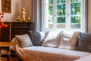 Una habitación con sofá, una estatua decorativa de un oso, un panel tallado en la pared y ventana con vista a follaje.