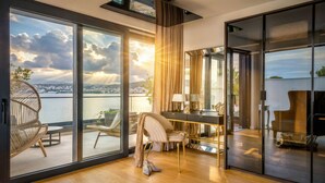 Ein modernes Zimmer mit einer großen Schiebeglaswand zu einem Balkon mit Blick auf ein Gewässer und eine Stadtlandschaft.