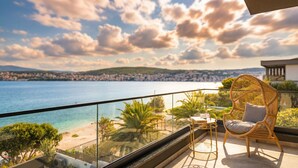 Ein Balkon mit Korbstuhl und Tisch, mit Blick auf einen Strand und das Meer.