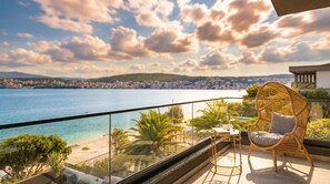 Ein Balkon mit Korbstuhl und Tisch, mit Blick auf einen Strand und das Meer.