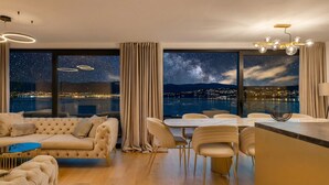 Ein modernes Wohnzimmer mit großem Fenster, einer Couch, einem Essbereich und einer Küchenzeile.