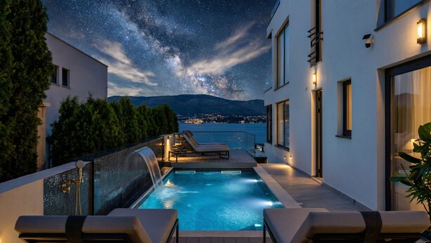 Ein Pool auf dem Dach, sternenklarer Nachthimmel, ein Berg im Hintergrund und eine Stadtlandschaft.