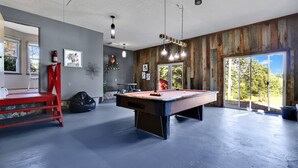 A pool table in a room with wooden walls, a red ladder, and a large window with a view of trees.