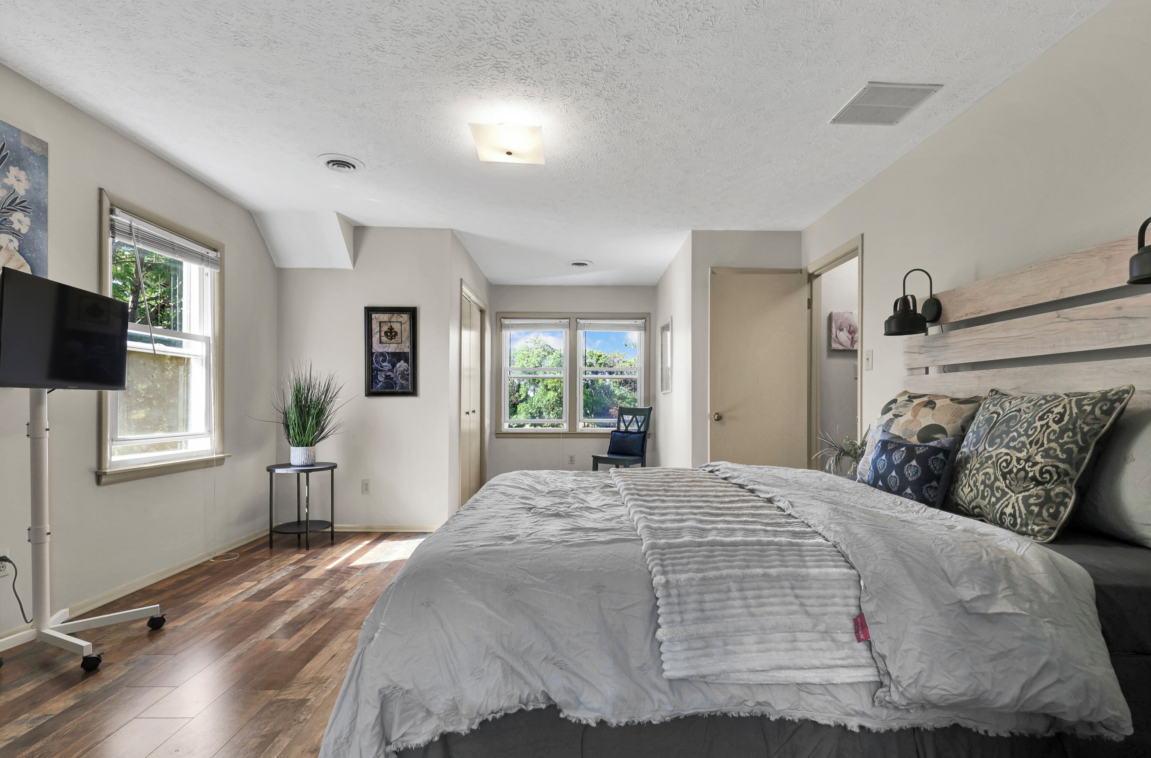 A bedroom with a bed, a TV, a potted plant, and a window with blinds.