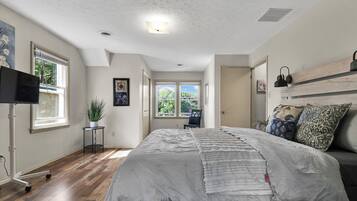 A bedroom with a bed, a TV, a potted plant, and a window with blinds.