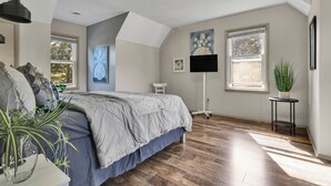 A bedroom with a bed, a standing lamp, a potted plant, and a window.