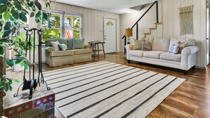 A spacious living room with two sofas, a striped rug, a ceiling fan, and a staircase.