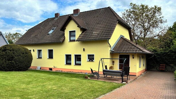 Une maison jaune avec un chemin en briques et une balançoire.