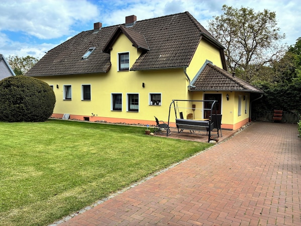 Ein gelbes Haus mit Pflasterweg und Schaukel.