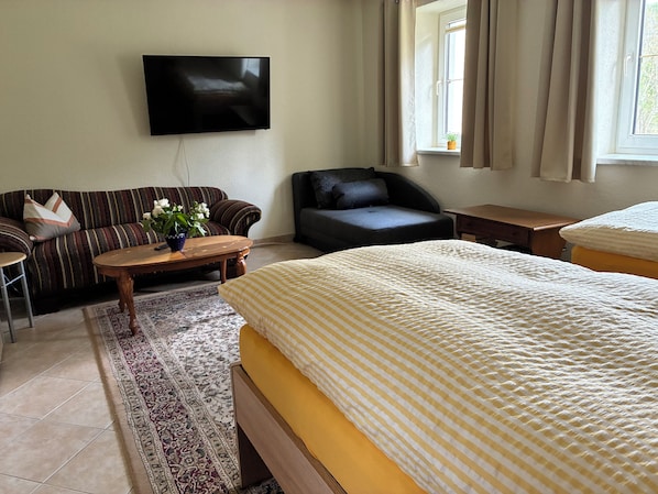 Ein Hotelzimmer mit Bett, Sofa, Sessel, Fernseher, Fenster und einem kleinen Tisch.