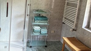 Une salle de bain avec une douche à parois de verre, un porte-serviettes en verre sur lequel sont pliés des serviettes, un banc en bois et un radiateur blanc.