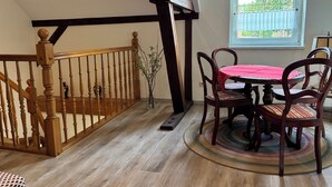 Un coin repas avec une table ronde, des chaises, un escalier en bois et une fenêtre donnant sur un beau paysage.