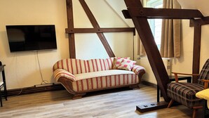 Une pièce comprenant un canapé, un fauteuil, un téléviseur fixé au mur et une fenêtre avec des rideaux.