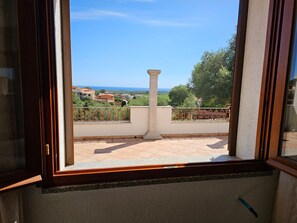A balcony with a stone column, tiled flooring, and a view of the sea and surrounding buildings. - Fml-greis01 in Malamor (Sassari)