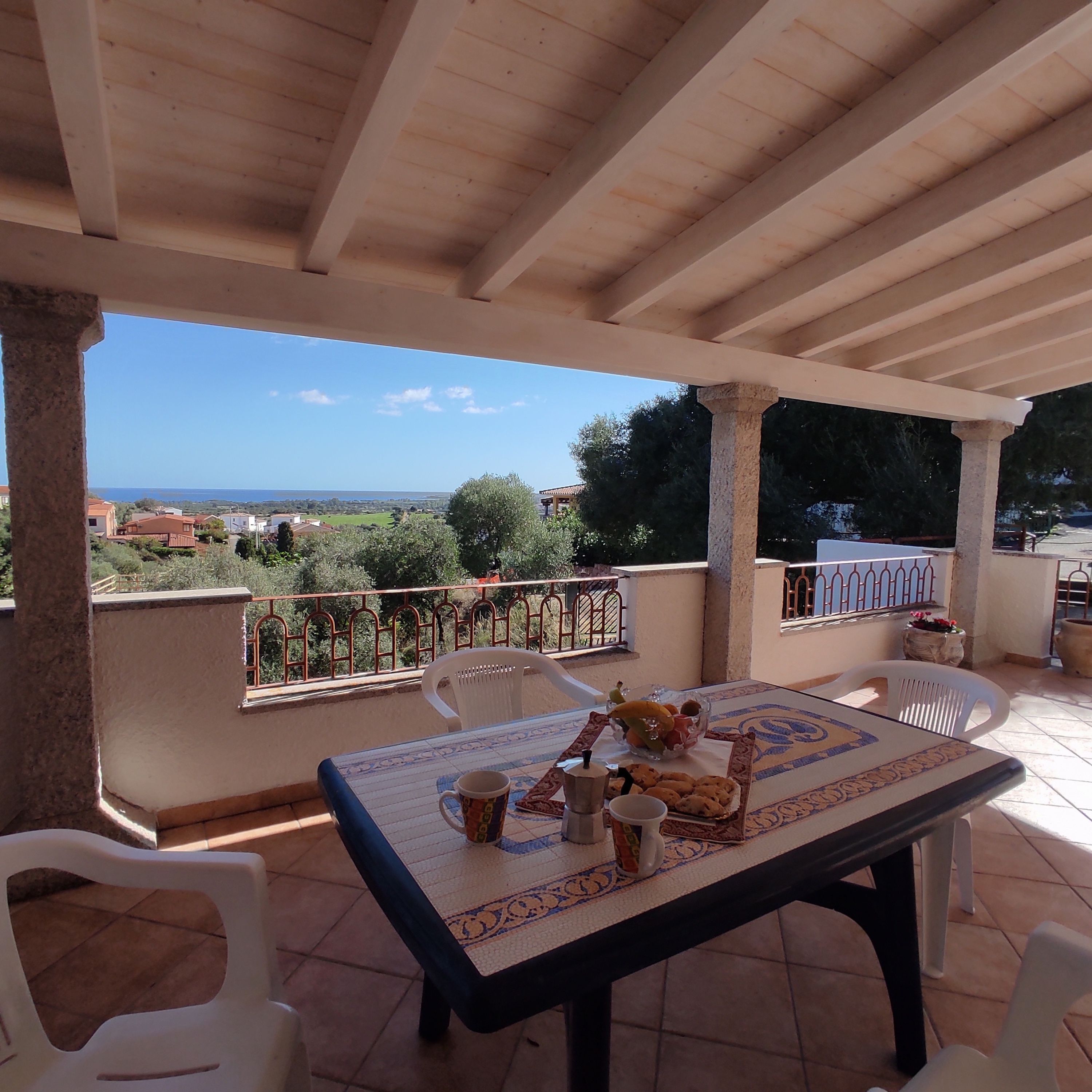 Un patio esterno coperto con tavolo apparecchiato per mangiare, sedie e vista sul paesaggio.