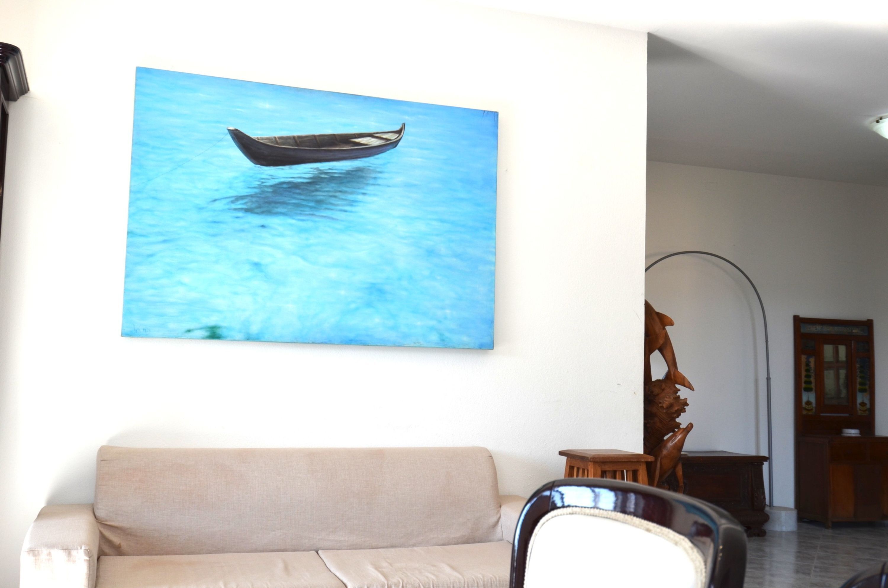 Una habitación con un sofá beige, una escultura de madera y un cuadro colgado en la pared que muestra un barco en el agua.