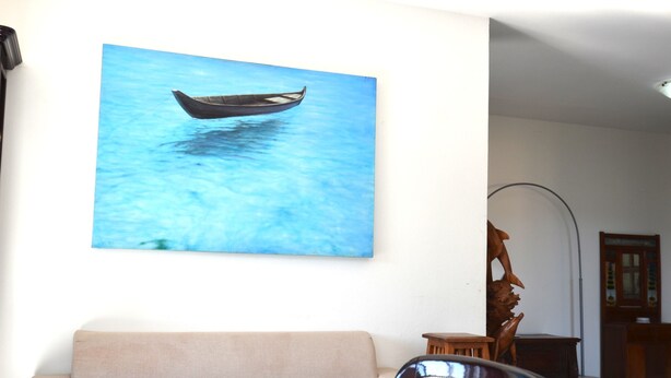 A room with a beige sofa, a wooden sculpture, and a wall-mounted painting of a boat on water. - Fst-jav01p1 in San Teodoro (San Teodoro)