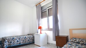 A bedroom with two single beds, a small white heater, a wooden nightstand, and a window with curtains. - Fst-jav01p1 in San Teodoro (San Teodoro)