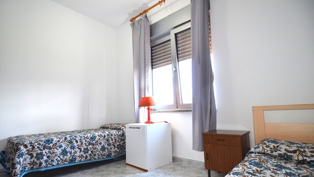 Ein Schlafzimmer mit zwei Einzelbetten, einer kleinen weißen Heizung, einem Holznachttisch und einem Fenster mit Vorhängen.