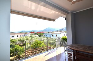 Un balcón con vista a edificios y montañas, una mesa y una silla.