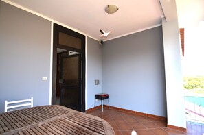 Ein Zimmer mit Holztisch, einem Stuhl, einer Tür, einem kleinen Hocker und einem Balkon mit Geländer.