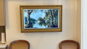 Quarto com duas cadeiras de madeira, um quadro de paisagem e uma porta branca.