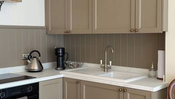A kitchen with beige cabinets, a white countertop, a kettle, a coffee maker, and a wooden stool.