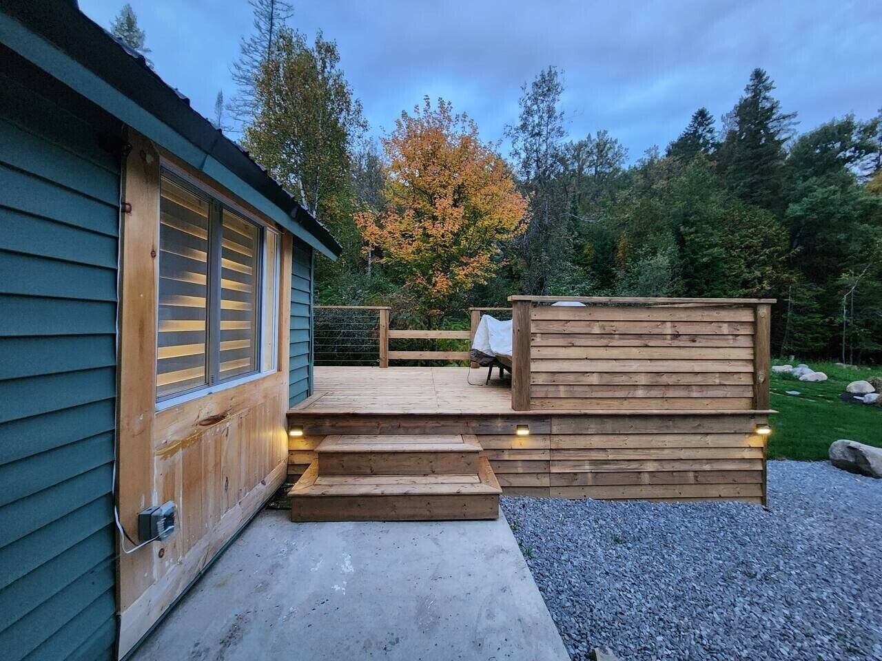 Eine Holzterrasse mit Stufen, die zu einem überdachten Bereich führen, umgeben von einer natürlichen Landschaft.
