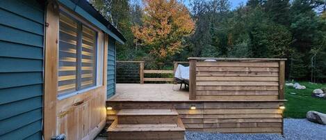Una terraza de madera con escalones que conducen a un espacio cubierto, rodeada de un paisaje natural.