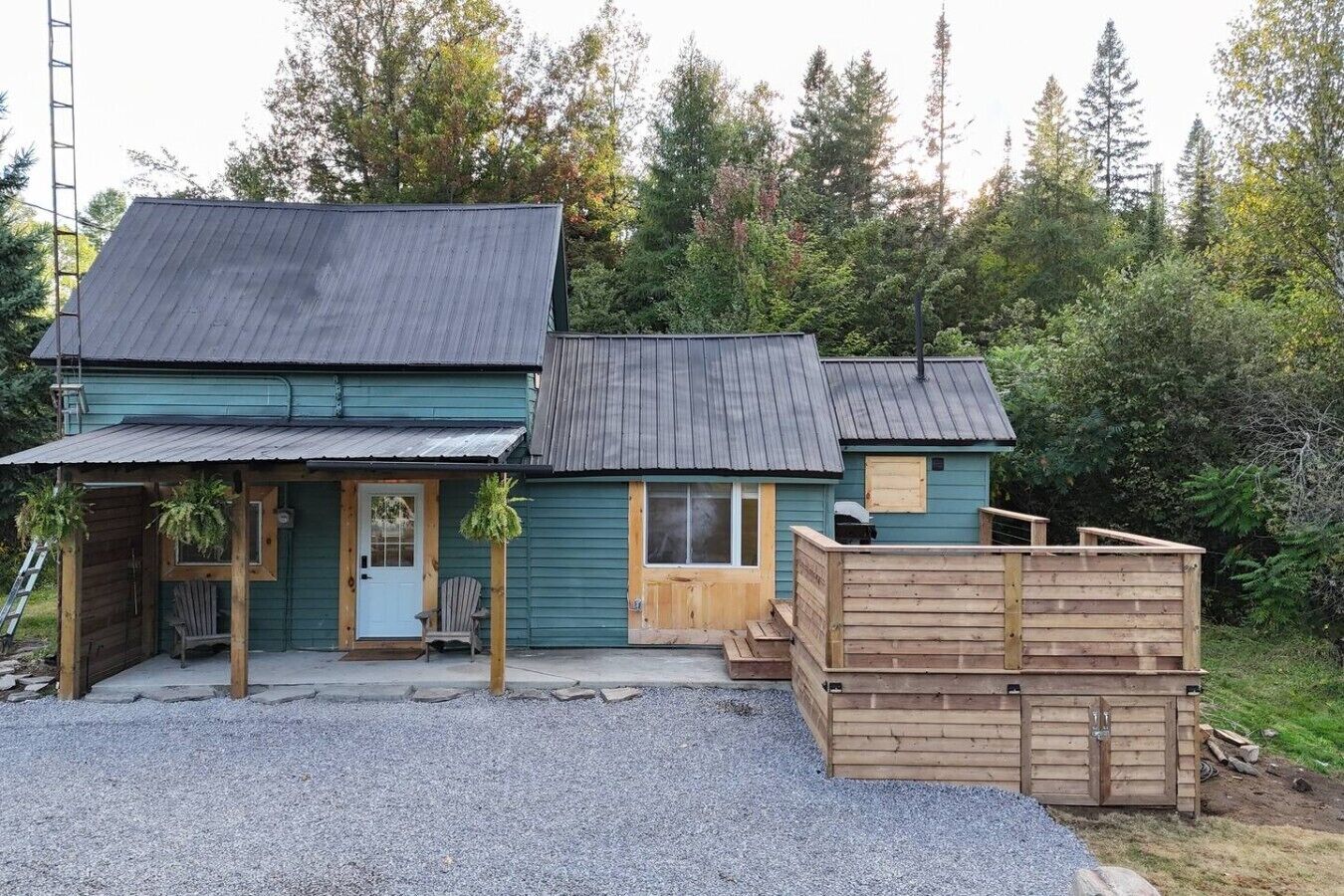 A two-story wooden cabin with a gravel driveway and a wooden deck.