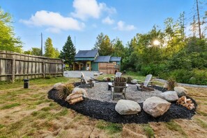 A cabin with a deck, surrounded by a fire pit area with seating, set in a forested landscape. - Bancroft Cottage | Hot Tub | Private 2 Acres (Harcourt)