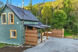 A small, single-story house with a sloped roof, a porch, and a gravel driveway.