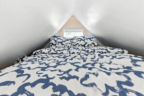 A bedroom with a sloped ceiling, a bed with patterned bedding, and a window with a view.
