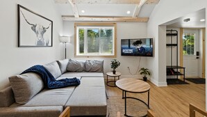 Una sala de estar moderna con un sofá, un televisor, una mesita y una ventana.