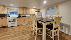 Una cocina con armarios de madera, una estufa, una mesa de comedor con sillas y una ventana con persianas.