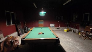 A pool table in a dimly lit room with a green felt surface, surrounded by walls with windows and a door. - South Baptiste Lake View | Boat Launch | Game Room (Hastings Highlands)