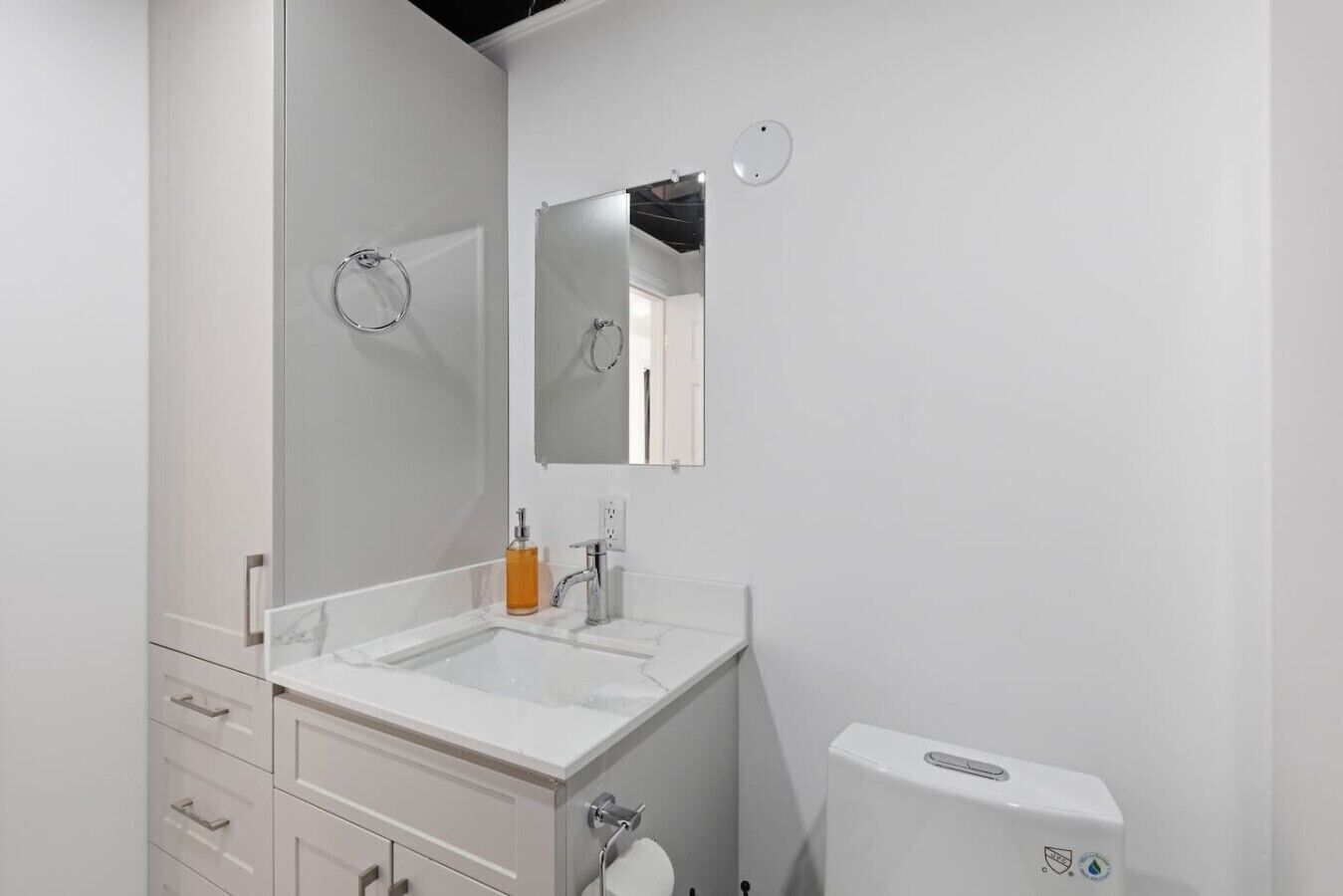 A modern bathroom with a white vanity, a large mirror, a toilet, and a sink.