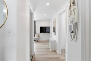 Um corredor com piso de madeira, uma cadeira, uma televisão e uma decoração com prancha de surf.