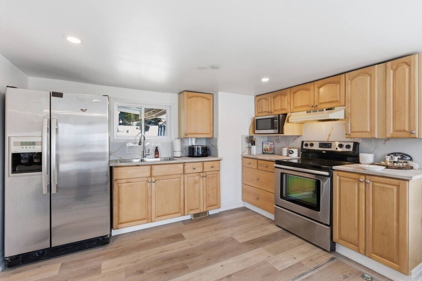 Una cocina moderna con electrodomésticos de acero inoxidable, armarios de madera y piso con patrón de espiga.
