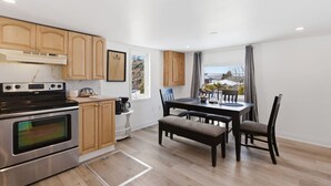 A modern kitchen with stainless steel appliances, wooden cabinets, and a dining area with a table and chairs. - South Baptiste Lake View | Boat Launch | Game Room (Hastings Highlands)