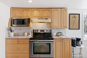 Una cocina con armarios de madera, microondas, estufa y cafetera.