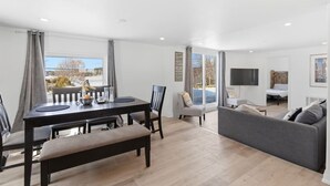 A modern living room with a dining area, a sofa, and a TV mounted on the wall. - South Baptiste Lake View | Boat Launch | Game Room (Hastings Highlands)