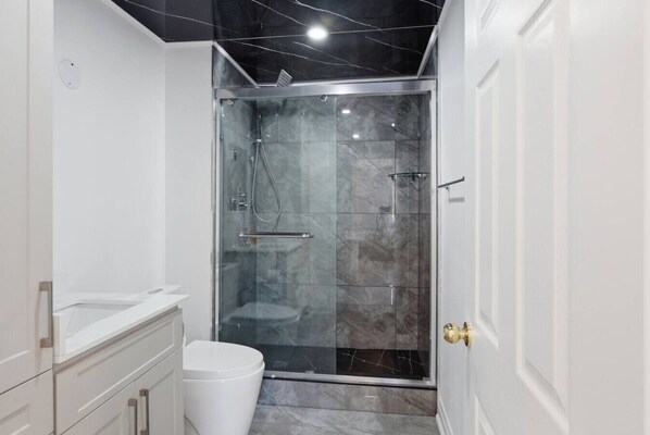 A modern bathroom with a glass-enclosed shower, white cabinetry, and a marble-tiled floor.