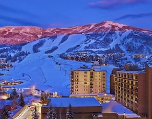 A hotel with a ski slope in the background, surrounded by snow-covered mountains.