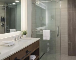 A modern bathroom with a glass shower enclosure, a large mirror, and a vanity with a sink and towel rack.