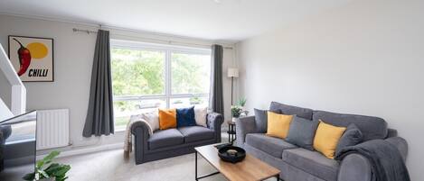 A modern living room with two grey sofas, a wooden coffee table, and a large window with curtains.