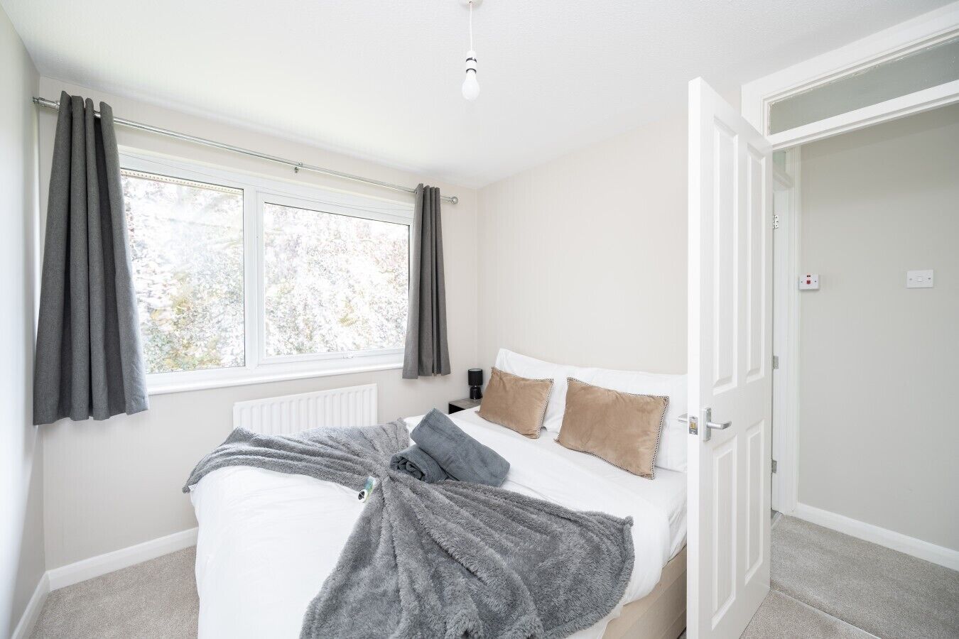 A bedroom with a bed, a radiator, a window with curtains, and a door.