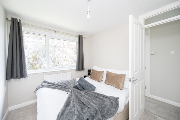 A bedroom with a bed, a radiator, a window with curtains, and a door.