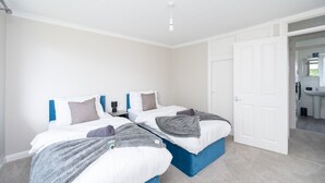 A hotel room with two beds, a white door, and a view into the bathroom. - 2 Bed Flat Free Parking Next To The Station (West Sussex)