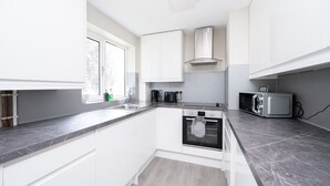 A modern kitchen with white cabinets, a built-in oven, a microwave, and a window providing natural light. - 2 Bed Flat Free Parking Next To The Station (West Sussex)